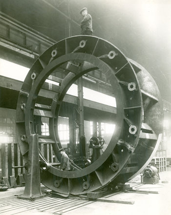 old black and white photo of a large wheel with a man standing on top of it